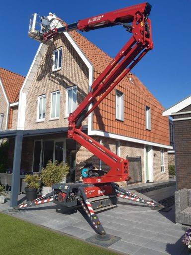 Een rode hoogwerker staat bij een huis met een stenen gevel en dakpannen.