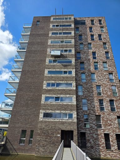 Modern gebouw met bakstenen façade en glazen balkons, omgeving met blauwe lucht.